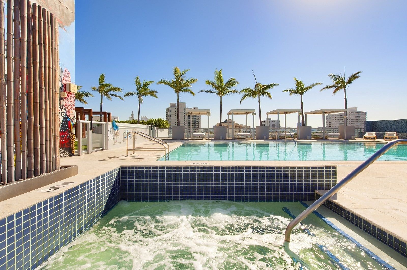 Une piscine avec un jacuzzi, des palmiers et une vue sur les gratte-ciel de la ville.