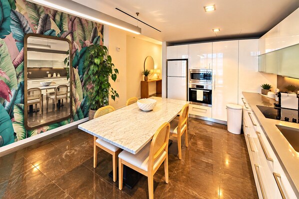 A modern kitchen with a marble countertop, stainless steel appliances, and a dining area with a large plant. - Luxury Suite w/ Rooftop Pool • Beach Steps Away (Miami Beach)
