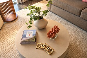 Une table basse ronde sur laquelle se trouvent un livre, une sculpture en corail et une plante dans un vase.