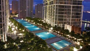 A rooftop pool area with multiple swimming pools, surrounded by high-rise buildings and trees. - Icon Brickell Condo with Bay Views (Miami)