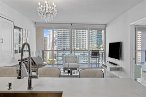 Una sala de estar moderna con un ventanal grande, una araña de cristal, un televisor de pantalla plana y un comedor.