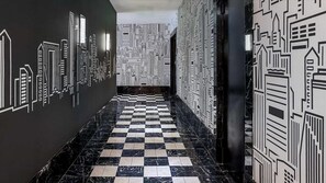 A hallway with a checkered floor and walls adorned with black and white cityscape patterns.