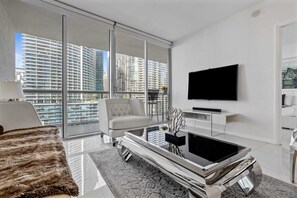 A modern living room with a large window, a flat-screen TV, a sofa, and a coffee table. - Icon Brickell W Hotel | Skyline View 1BR Suite (Miami)