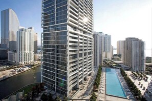 Un edificio de gran altura con fachada de vidrio, una piscina y un río al fondo.