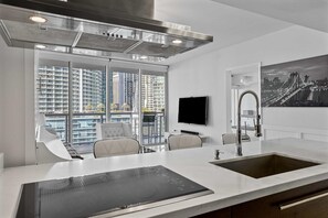 A modern kitchen with a large island, a built-in oven, and a large window with a city view. - Icon Brickell W Hotel | Skyline View 1BR Suite (Miami)