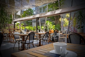 An outdoor café with wooden tables and chairs, a glass of water, and a menu on the table.