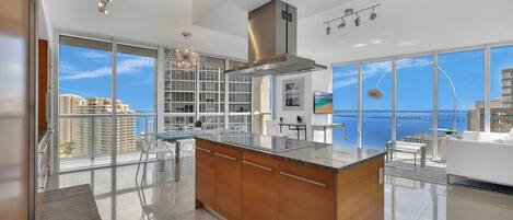 A modern kitchen with a large island, stainless steel appliances, and a view of the sea.