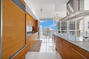 A modern kitchen with wooden cabinets, a stainless steel range hood, and a large window overlooking a cityscape.