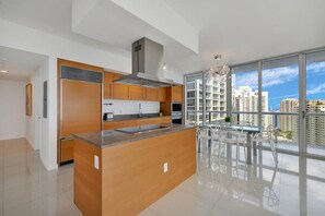 A modern kitchen with a central island, wooden cabinets, and a large window offering a city view.