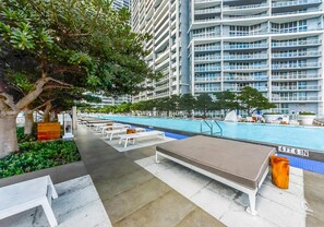 A rooftop pool area with lounge chairs and a small table, surrounded by greenery and tall buildings. - Panoramic Bay View 2BR Condo · Icon Brickell (Miami)