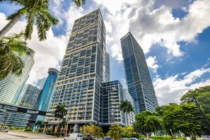 A modern high-rise building with a grid of windows and balconies, surrounded by palm trees and other greenery. - Panoramic Bay View 2BR Condo · Icon Brickell (Miami)