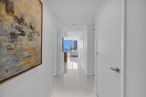 A hallway with a large abstract painting on the left, leading to a room with a view of the city.