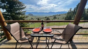 A balcony with two chairs and a table, overlooking a scenic landscape with mountains and trees. - Moonlight Ridge Cabin (Ennis)