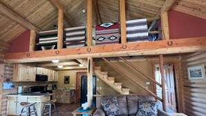 A log cabin interior with a kitchen, dining area, and a sofa with decorative pillows. - Moonlight Ridge Cabin (Ennis)