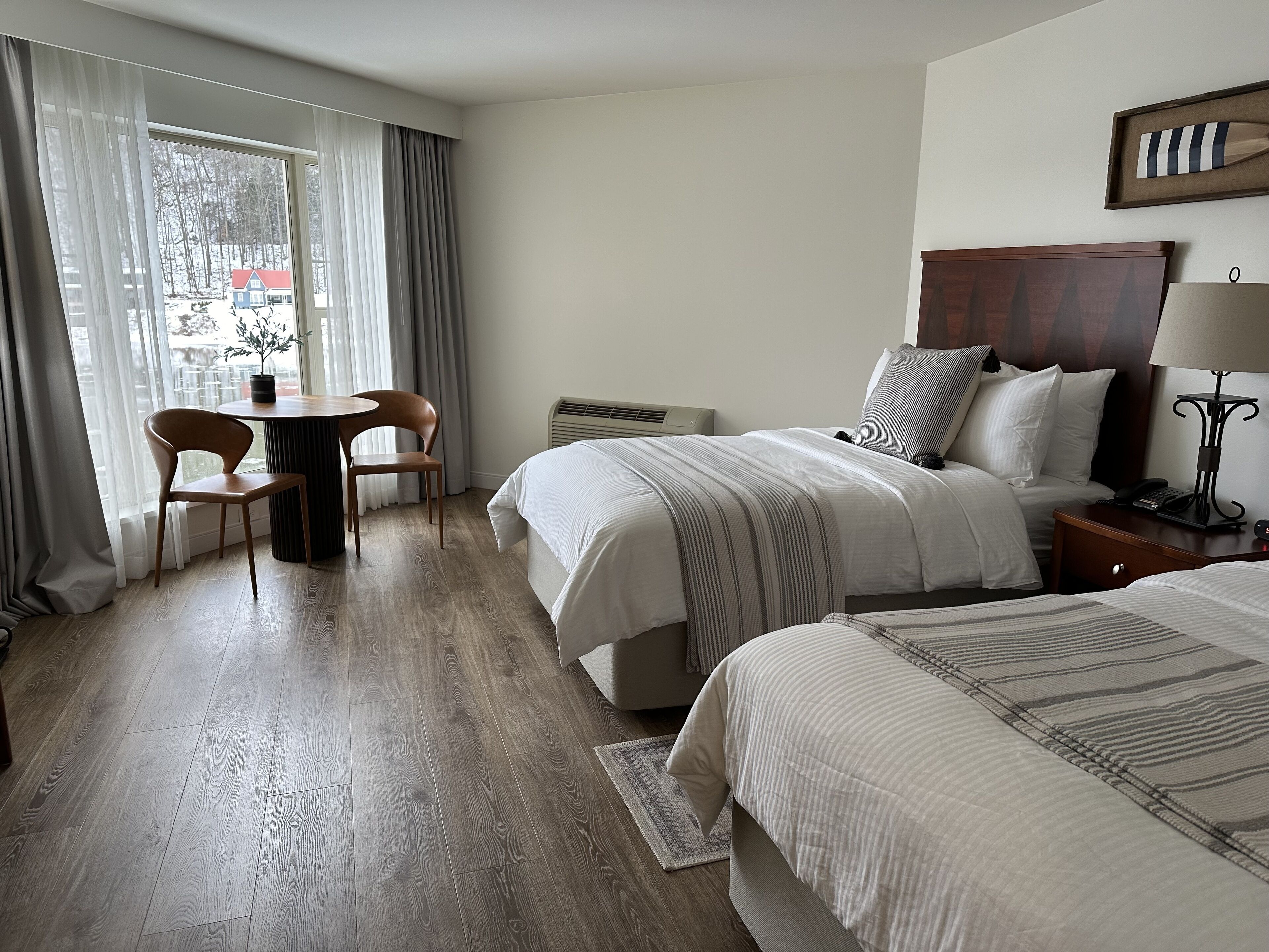 Una camera d'albergo con un letto, un comodino, una lampada e vista su un paesaggio innevato dalla finestra.