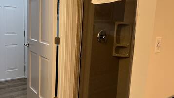 A bathroom with a glass shower door, a white towel hanging on the door, and a toilet paper holder on the wall.