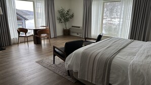 A modern hotel room with a large bed, a desk, a chair, and a view of a snowy landscape through the windows. - Foxburg Inn (Foxburg)