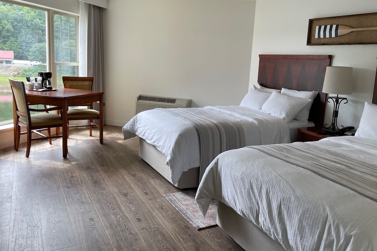 A hotel room with two beds, a dining table, and a view of the outdoors.