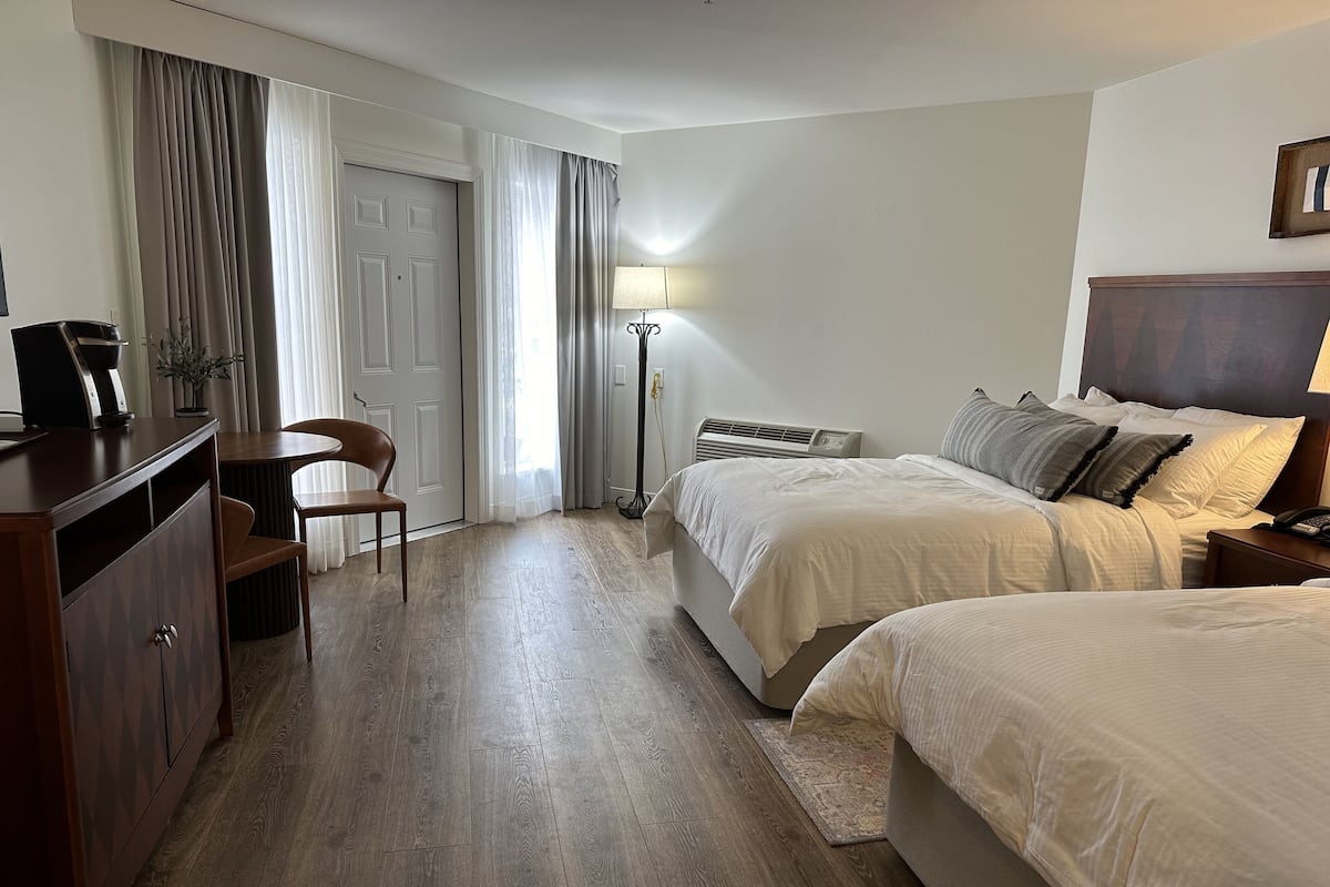 A hotel room with two beds, a desk, a chair, a lamp, and a wardrobe.