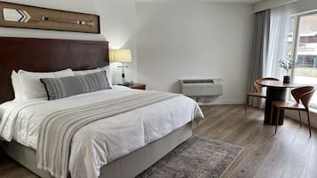 A hotel room with a large bed, a bedside table with a lamp, a small table with chairs, and an air conditioning unit.