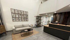 A modern lobby with a grey sofa, a black coffee table, a reception desk, and a wall with framed botanical illustrations. - Foxburg Inn (Foxburg)