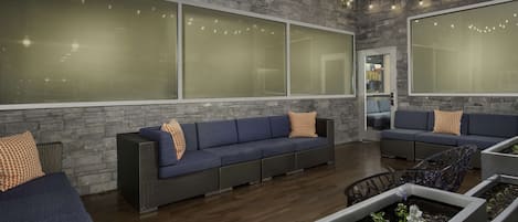 A modern lounge area with grey brick walls, large windows, and a blue sofa set.