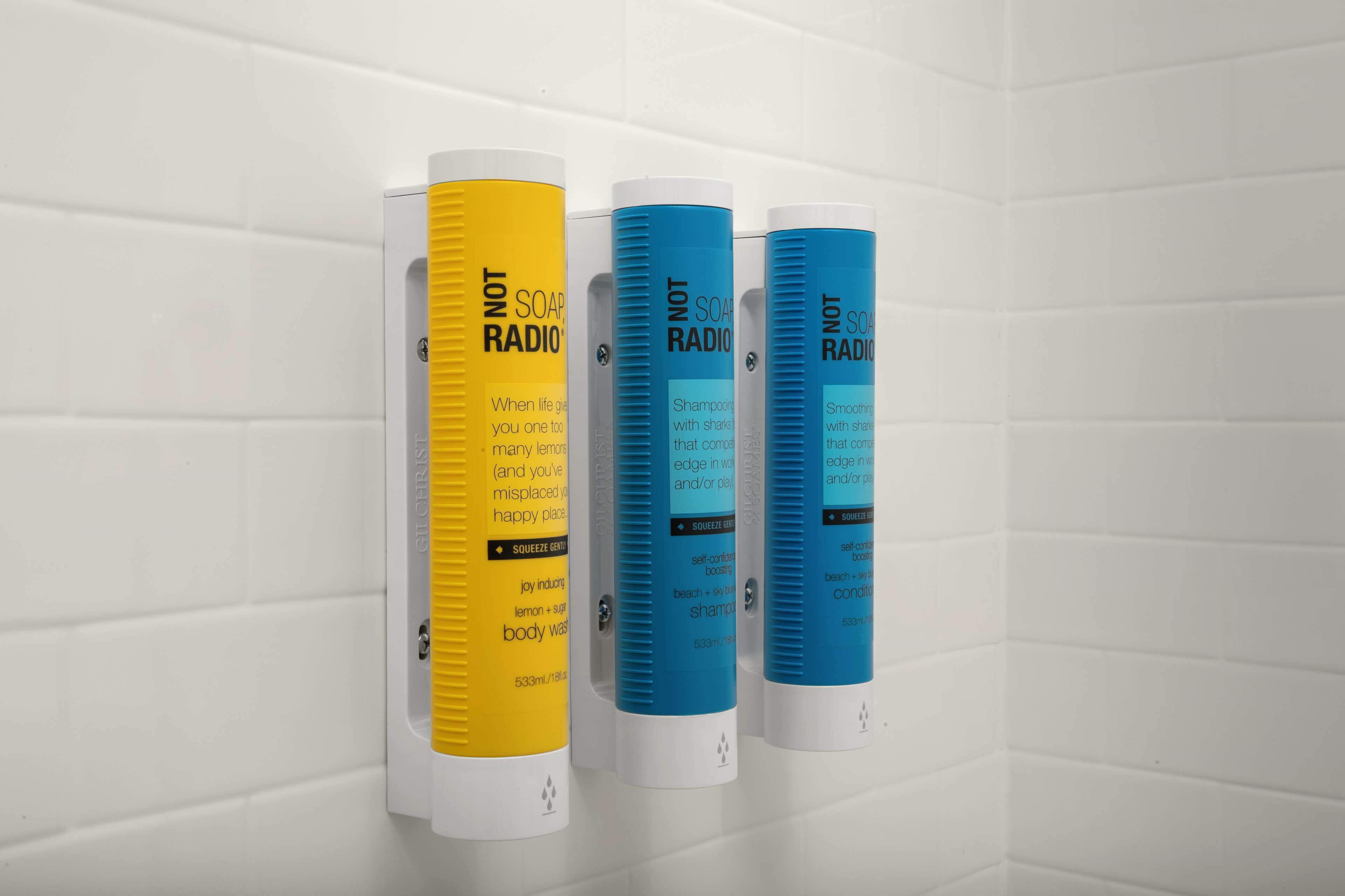 Three bottles of Not Soap Radio shampoo on a white tiled wall.