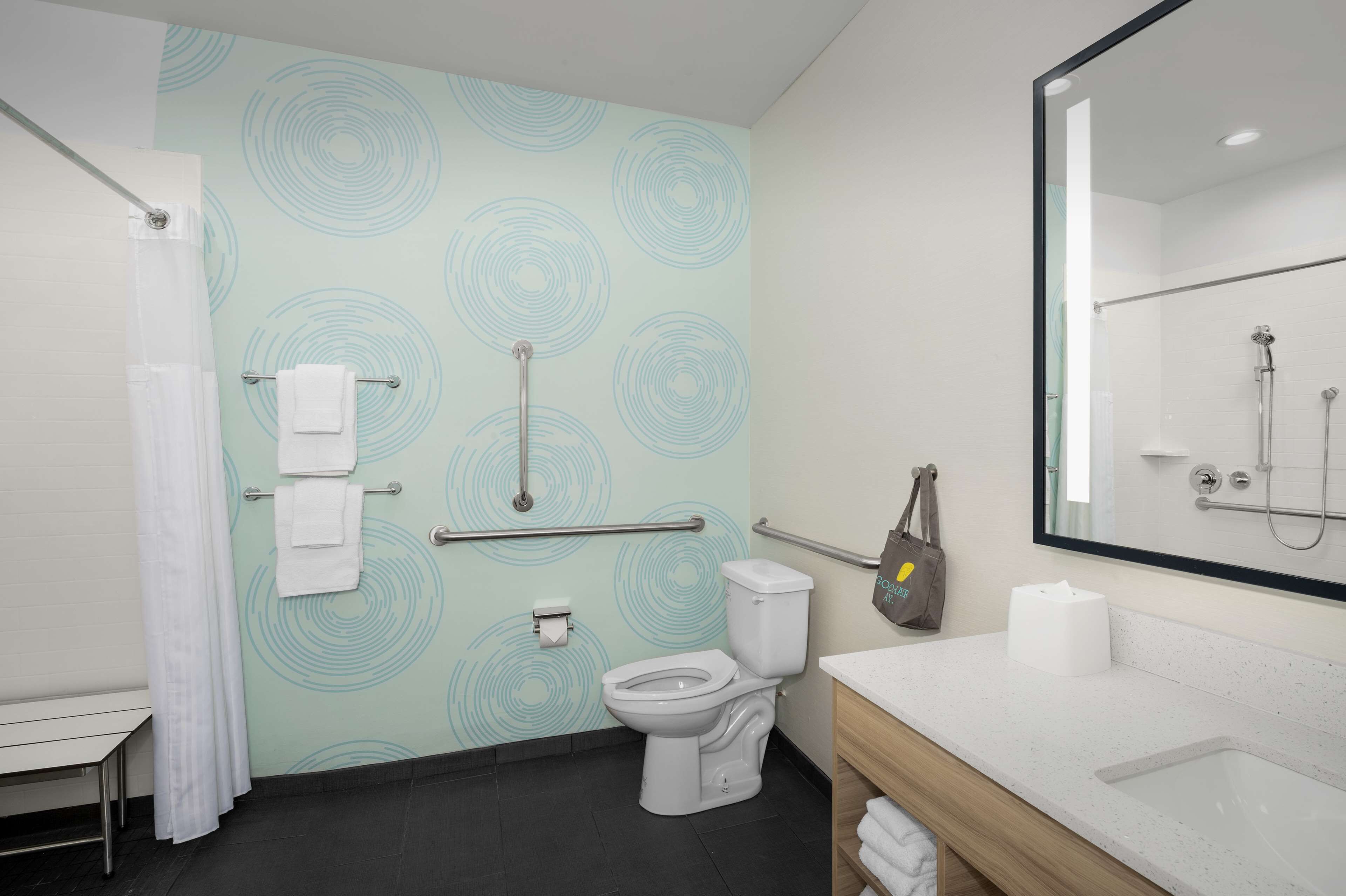 Een moderne badkamer met toilet, wastafel en douche. Het heeft een lichtblauwe behang, een wit toilet en een grote spiegel boven de wastafel.