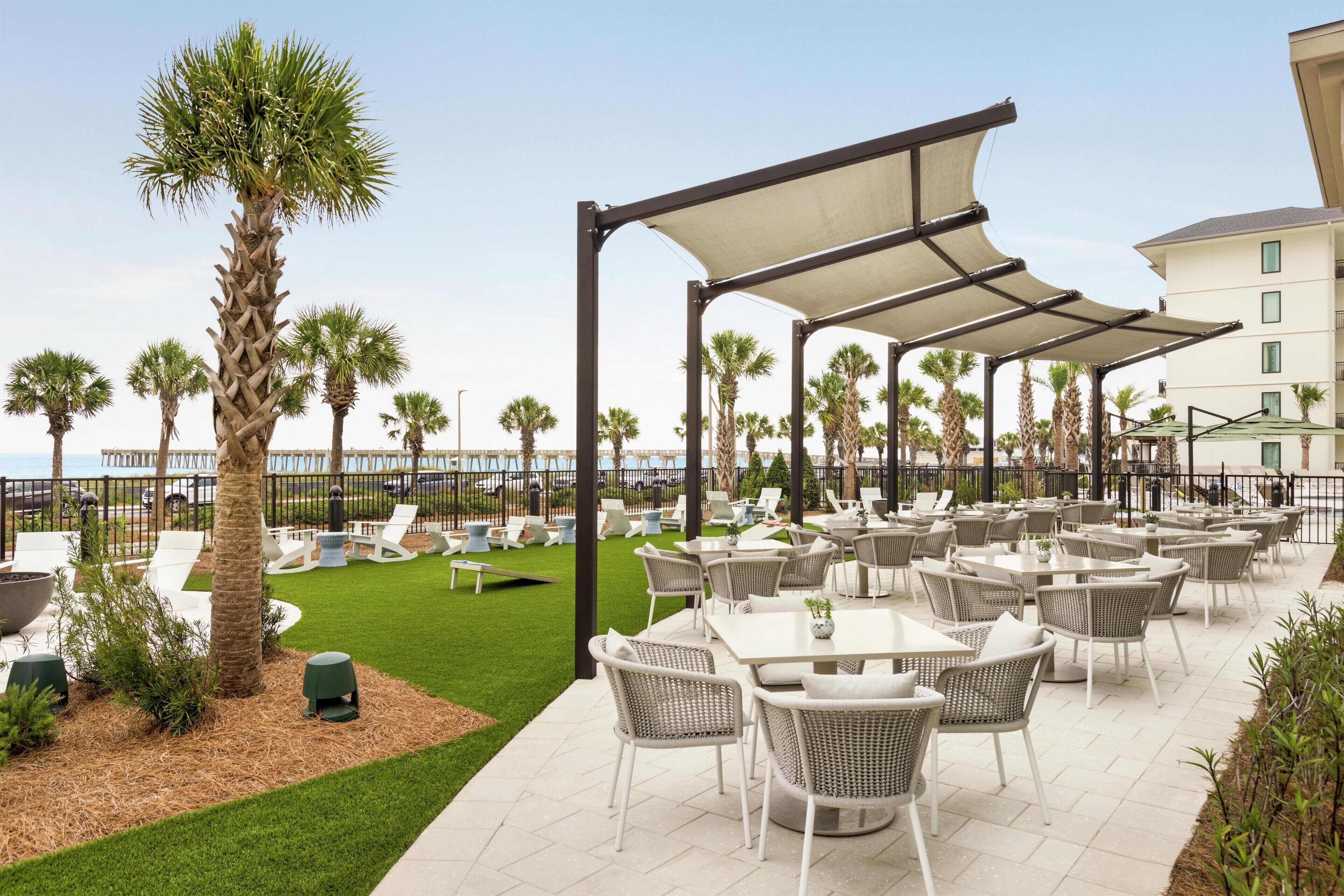 Un patio al aire libre con mesas y sillas, palmeras y vistas al mar.