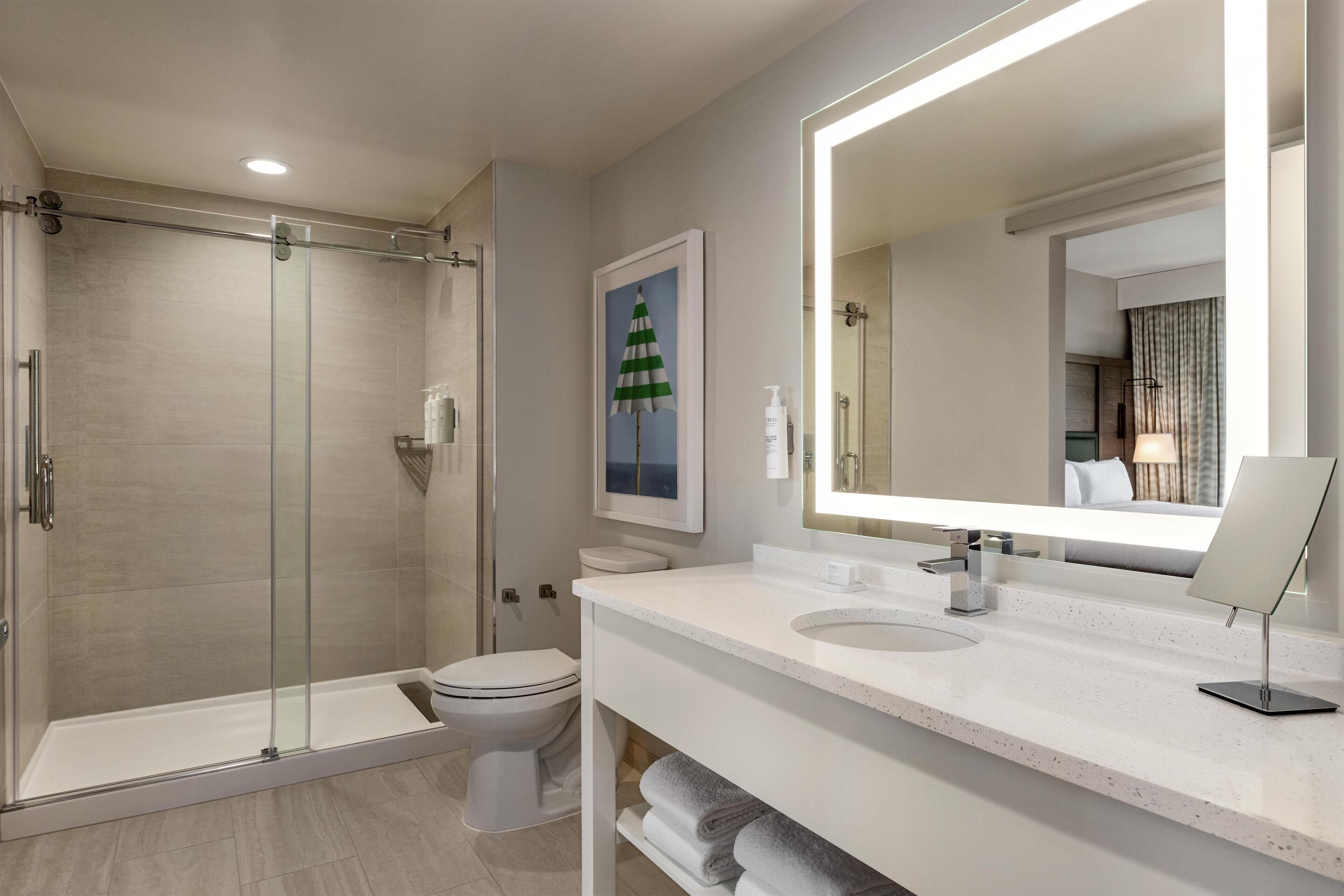 A modern bathroom with a glass-enclosed shower, a toilet, and a large mirror.