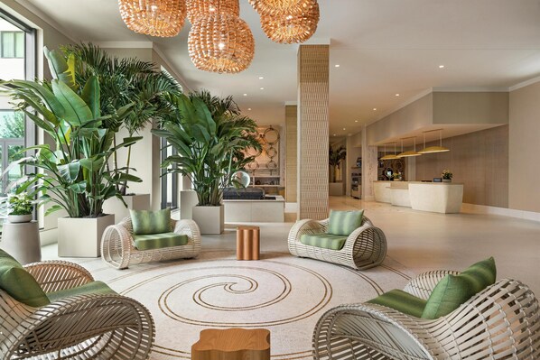 A spacious lobby with wicker furniture, large potted plants, and a central spiral rug.