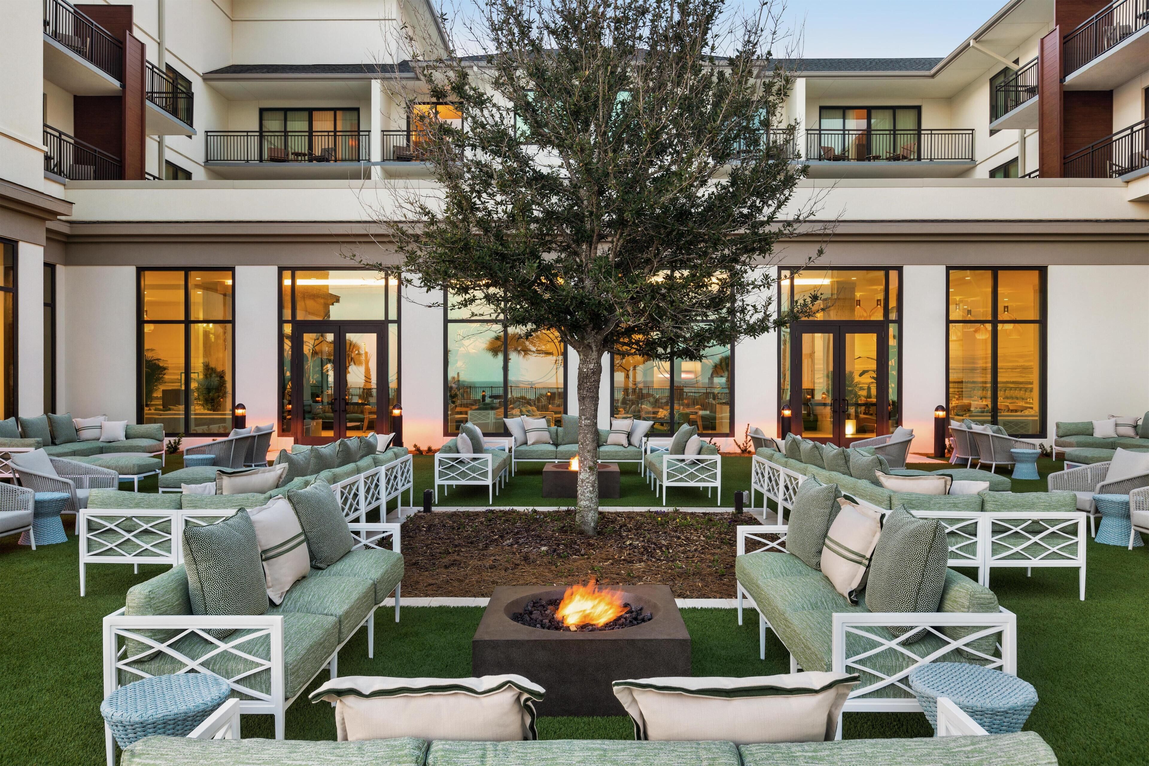 A courtyard with outdoor seating, a central fire pit, and a tree.