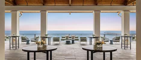 A terrace with round tables and chairs, a view of the sea, and a wooden ceiling.
