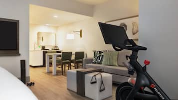 Una habitación de hotel moderna con una cama, un escritorio, un sofá y una bicicleta estática Peloton.