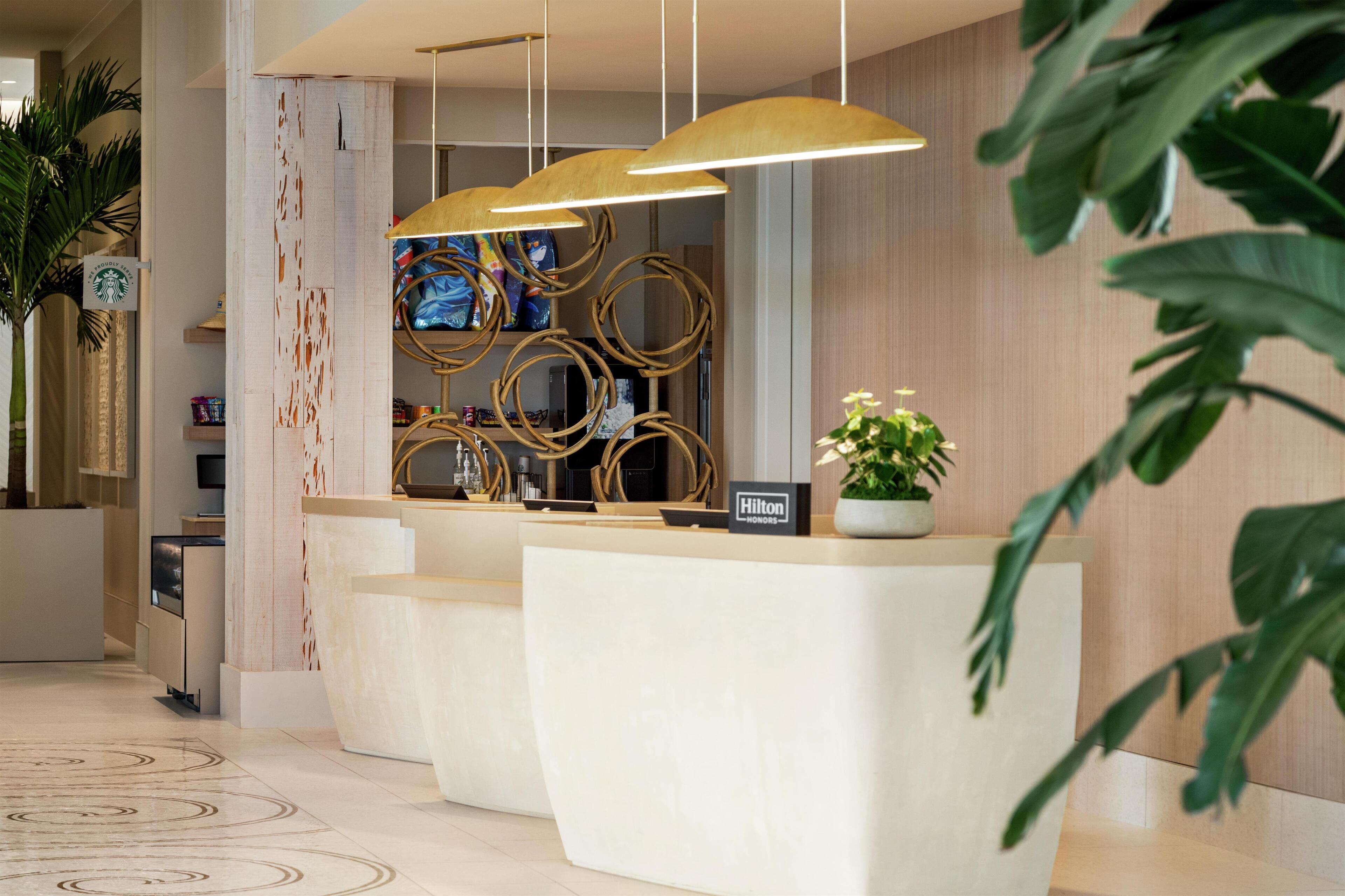 Un espace d’accueil d’hôtel au design moderne, comprenant un comptoir d’accueil blanc, un panneau indiquant « Hilton Honors » et un mur décoratif orné de motifs circulaires.