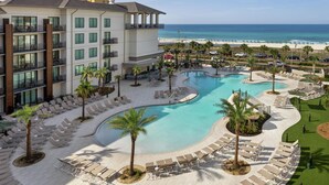 A resort pool area with lounge chairs, palm trees, and a view of the beach. - Embassy Suites by Hilton Panama City Beach Resort (Panama City Beach)