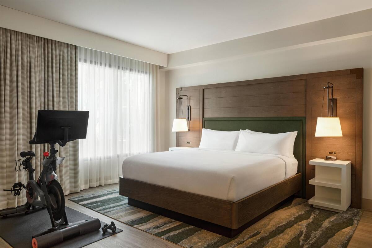 A hotel room with a large bed, a TV, exercise equipment, and a wooden headboard.