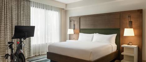 Una habitación de hotel con una cama grande, televisión, equipo de ejercicio y un cabecero de madera.