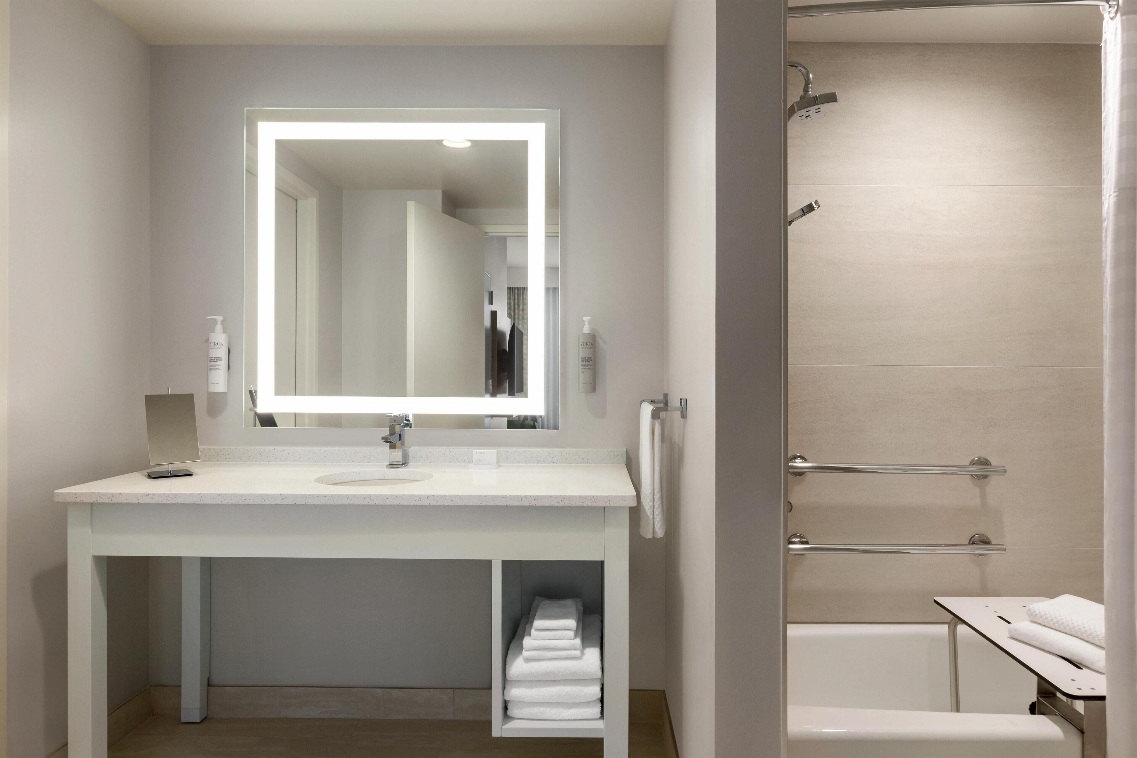 Une salle de bain moderne avec un grand miroir, un lavabo blanc et un espace douche.