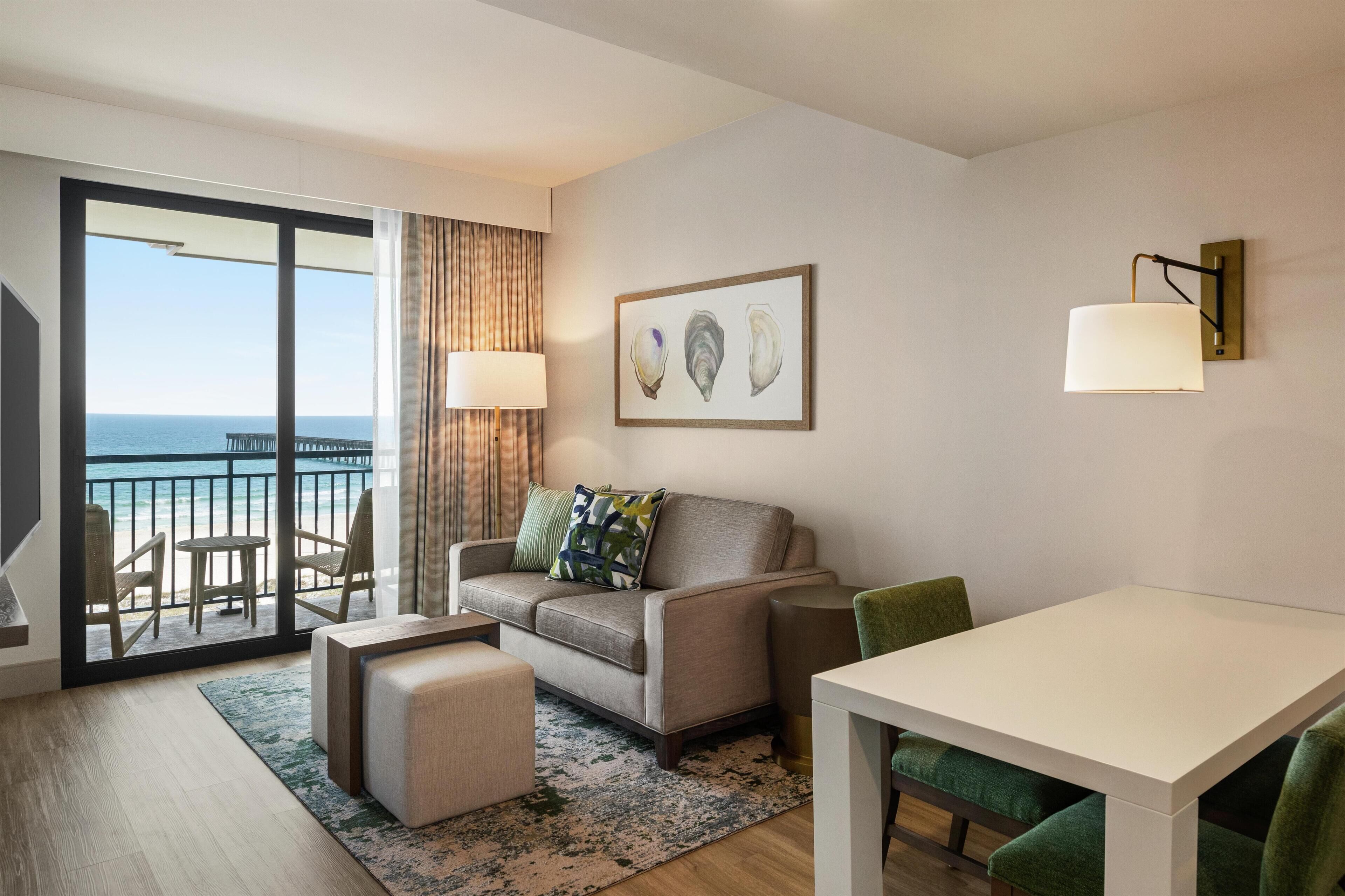A modern hotel room with a balcony, a sofa, a table, and a view of the sea.