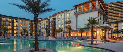 A hotel with a swimming pool, multiple balconies, and palm trees.