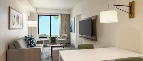 Quarto de hotel moderno com sofá, cadeiras, mesa de jantar, televisão e uma grande janela com vista para o exterior.