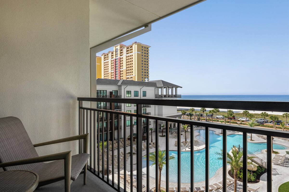 A balcony with a view of a swimming pool and a high-rise building in the background.