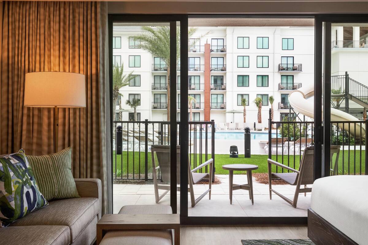 A hotel room with a view of a pool, outdoor seating, and a building with balconies.