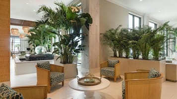 A spacious lobby with wicker furniture, large potted plants, and a modern design.