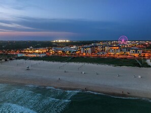 A beachfront hotel with a Ferris wheel, sandy beach, and ocean waves.