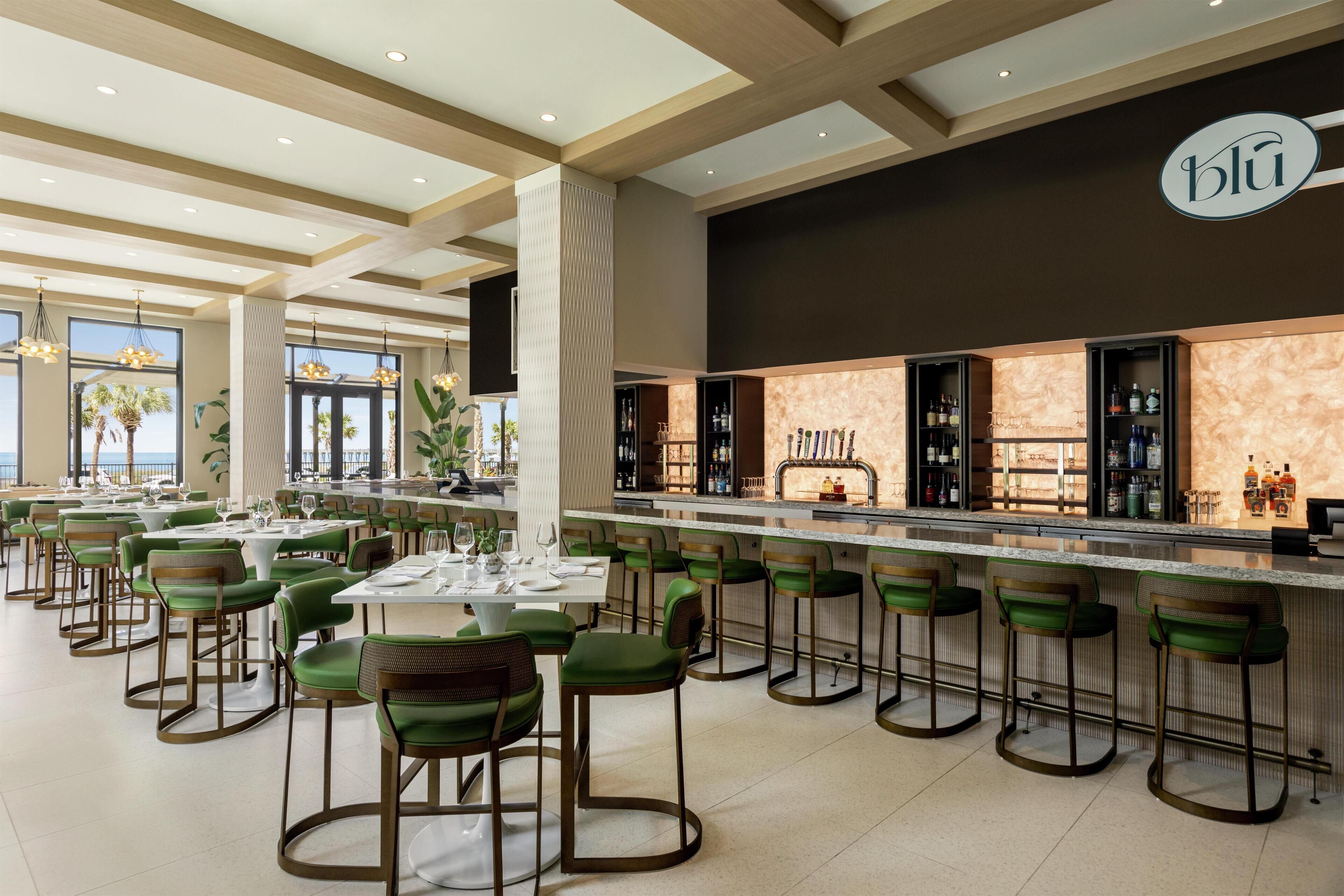 A modern restaurant with green bar stools, a marble counter, and a view of the ocean.