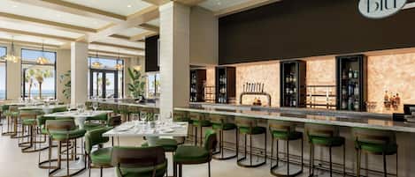 A modern restaurant with green bar stools, a marble counter, and a view of the ocean.