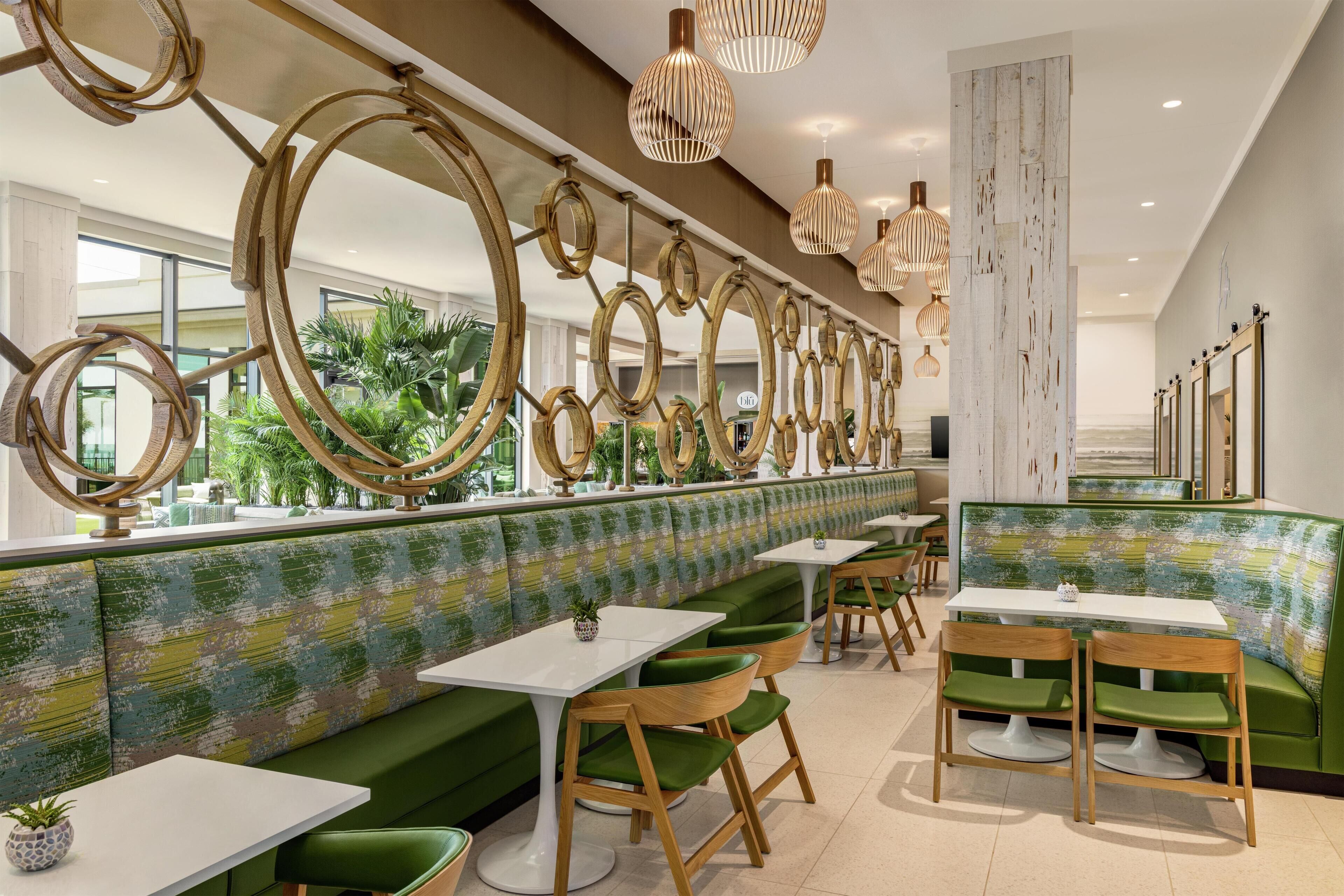 Een restaurant met groene banken, witte tafels en een decoratief plafond met ronde elementen.