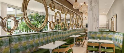 A restaurant with green booths, white tables, and a decorative ceiling with circular elements.